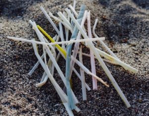 A number of plastic coloured straws in a pile on a beach.