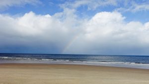 A wide sandy beach with a dark blue sea, large white clouds and a little blue sky