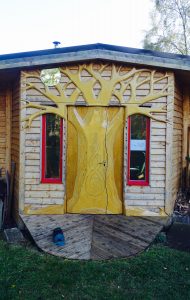 A wooden shed with the door decorated with a large carved wooden tree.