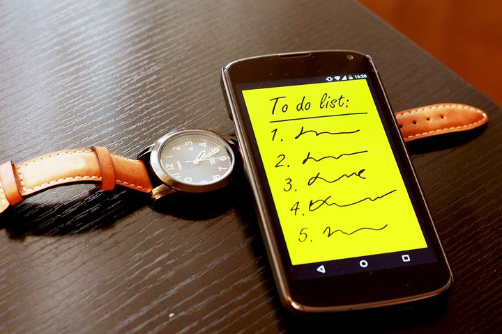 A phone with text on the screen "to do list" numbers and representational text. A watch lies under the phone.