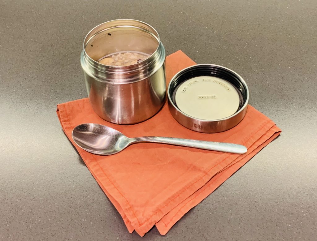 Metal round container with porridge, napkin and spoon