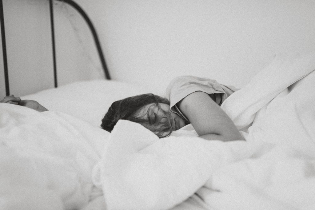 Black and white image of a women asleep in a bed with white covers.