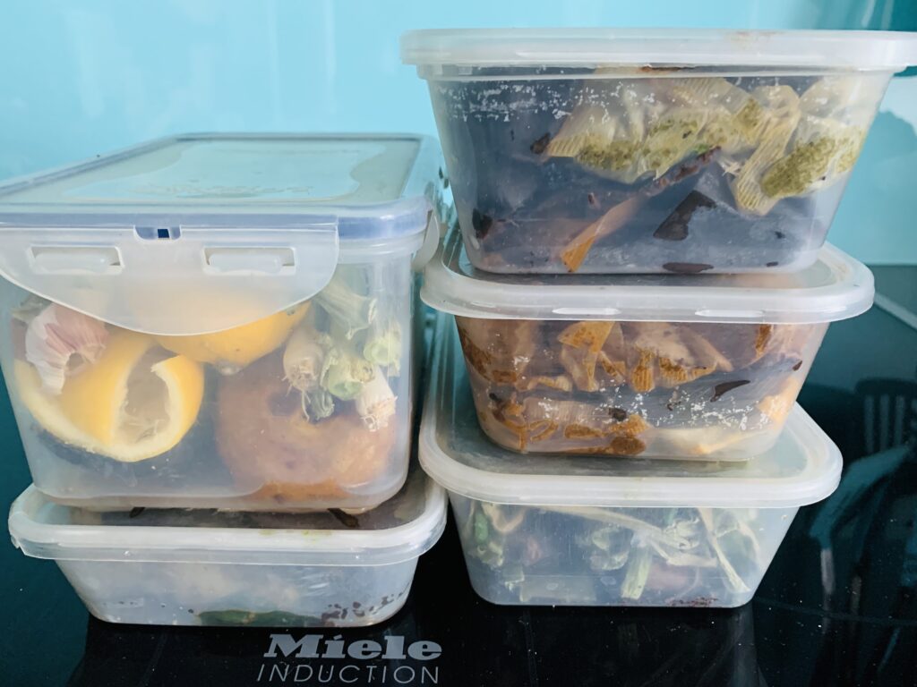 Five plastic tupperware tubs stocked up with food waste inside.