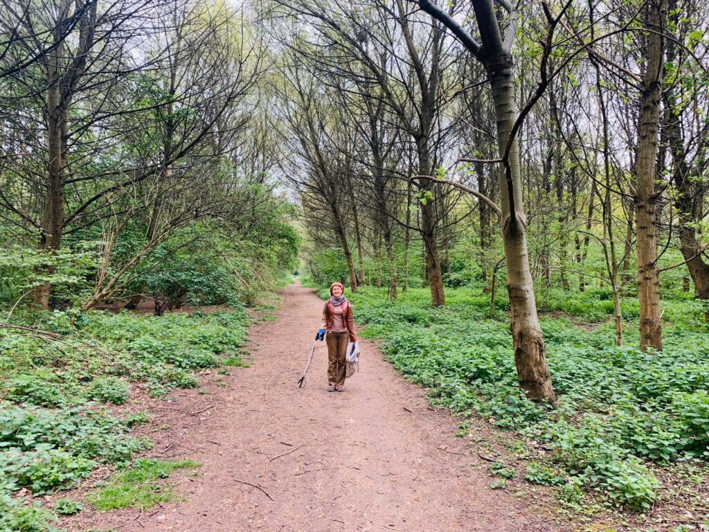 Path in a woodland. Woman holding litter pick stick and bag.