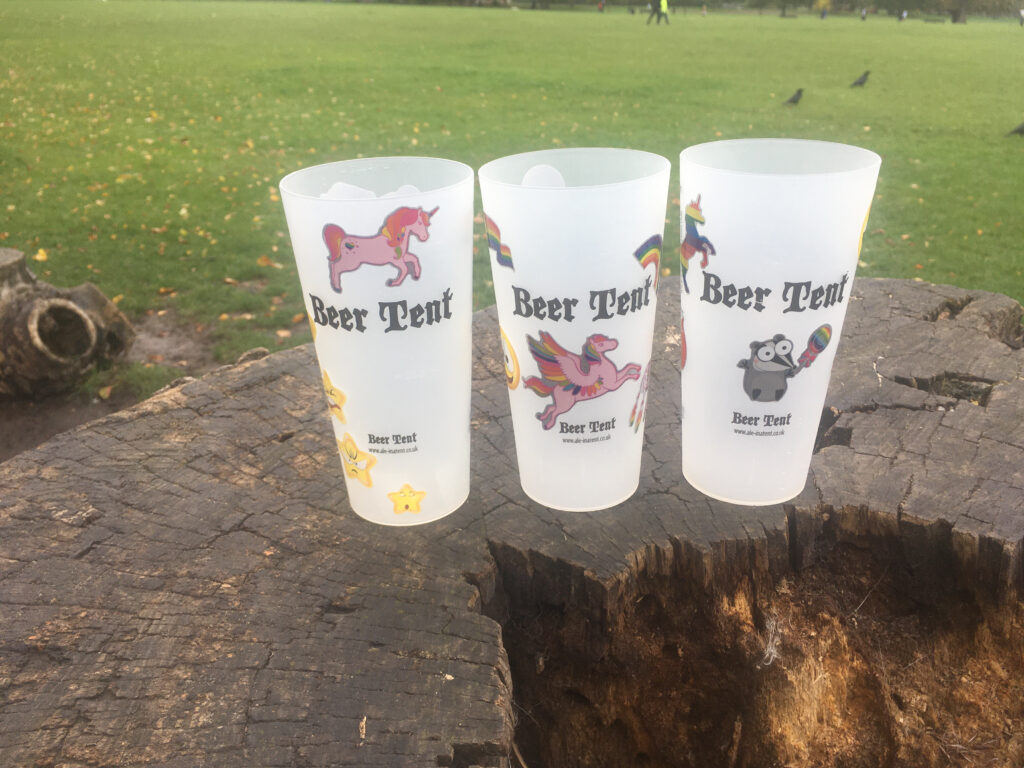 Three reusable pint glass cups on a tree stump with grass in the background