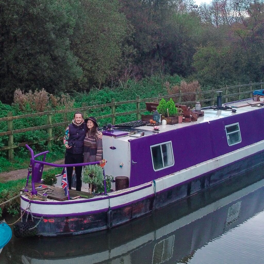 A couple stood on the prow of a narrow boat on a canal.