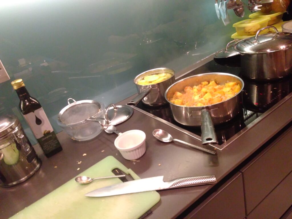 A kitchen hob and work surface with 3 pans a chopping board and knife.