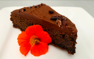 Chocolate cake slice on white plate with orange nasturtium flower