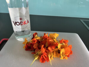 Bottle of vodka, pile of nasturtium flowers on a white chopping board.